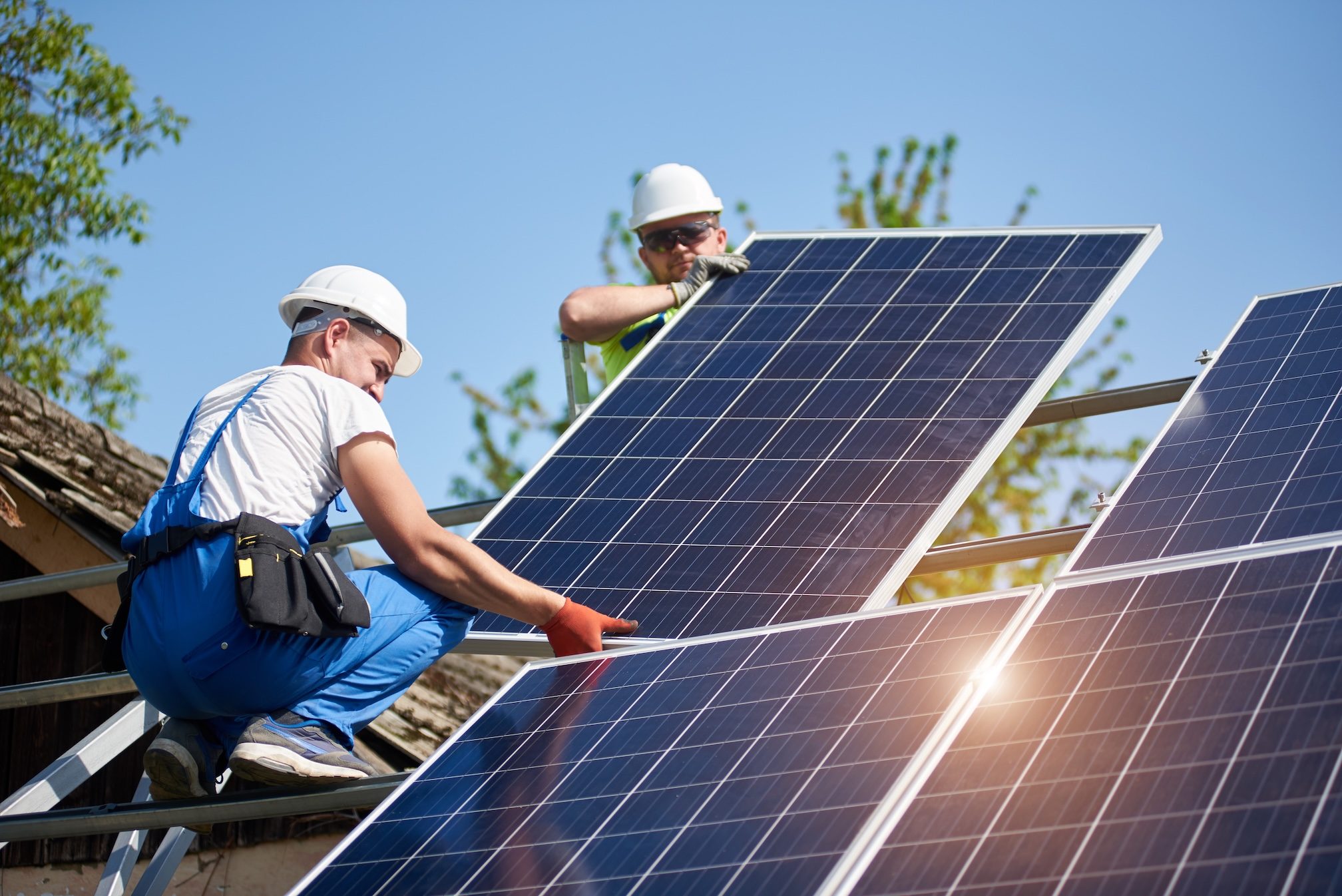Dwóch instalatorów w hełmach montujących panele PV na dachu
